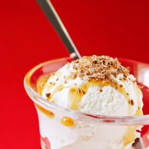 Delicious vanilla ice cream sundae with caramel and chocolate shavings in a glass cup.